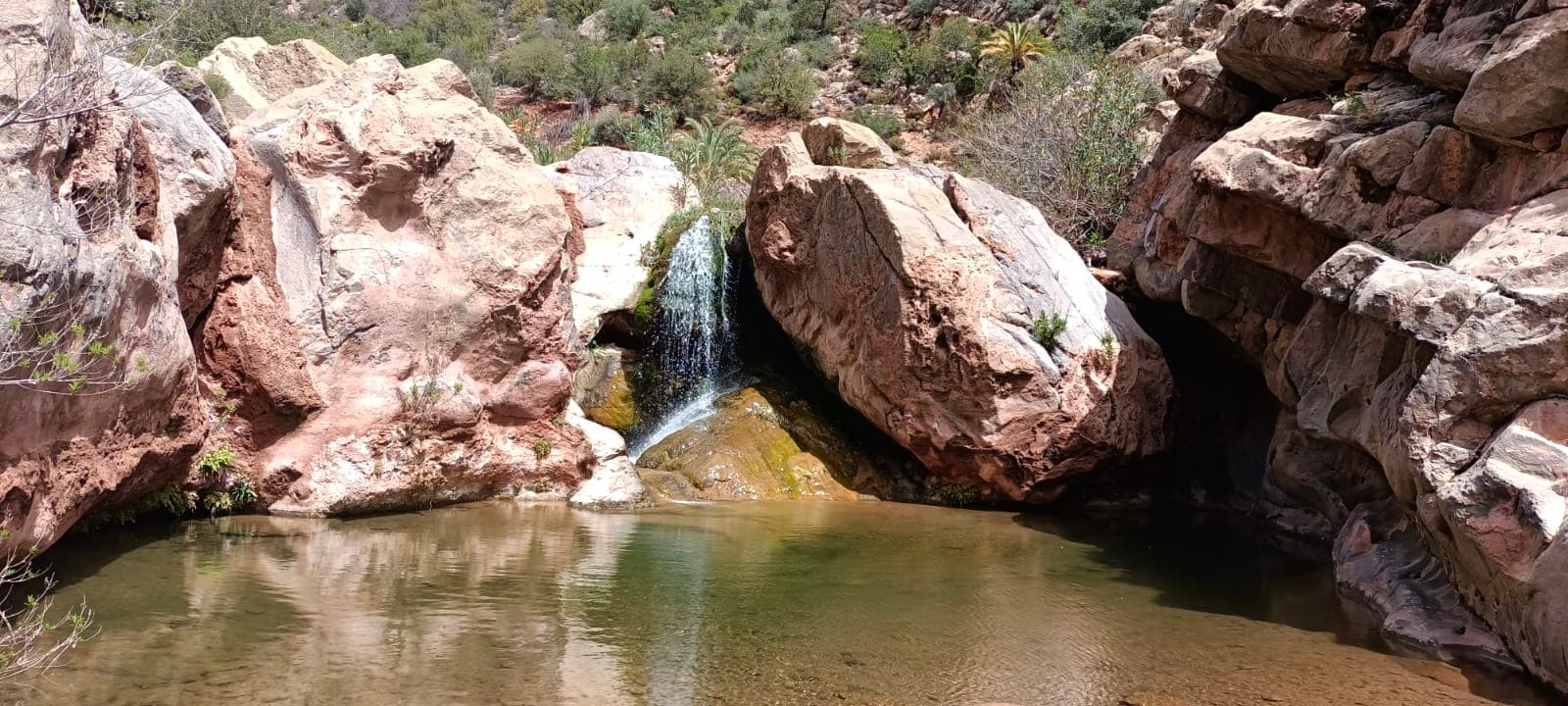 Small waterfall flowing between boulders into a calm natural pool